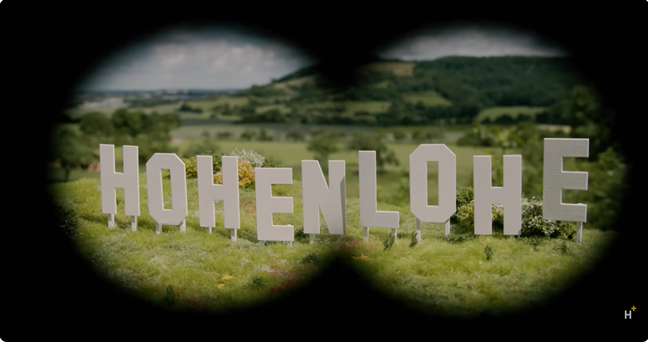 Schriftzug „Hohenlohe“ in der Landschaft, gesehen durch ein Fernglas
